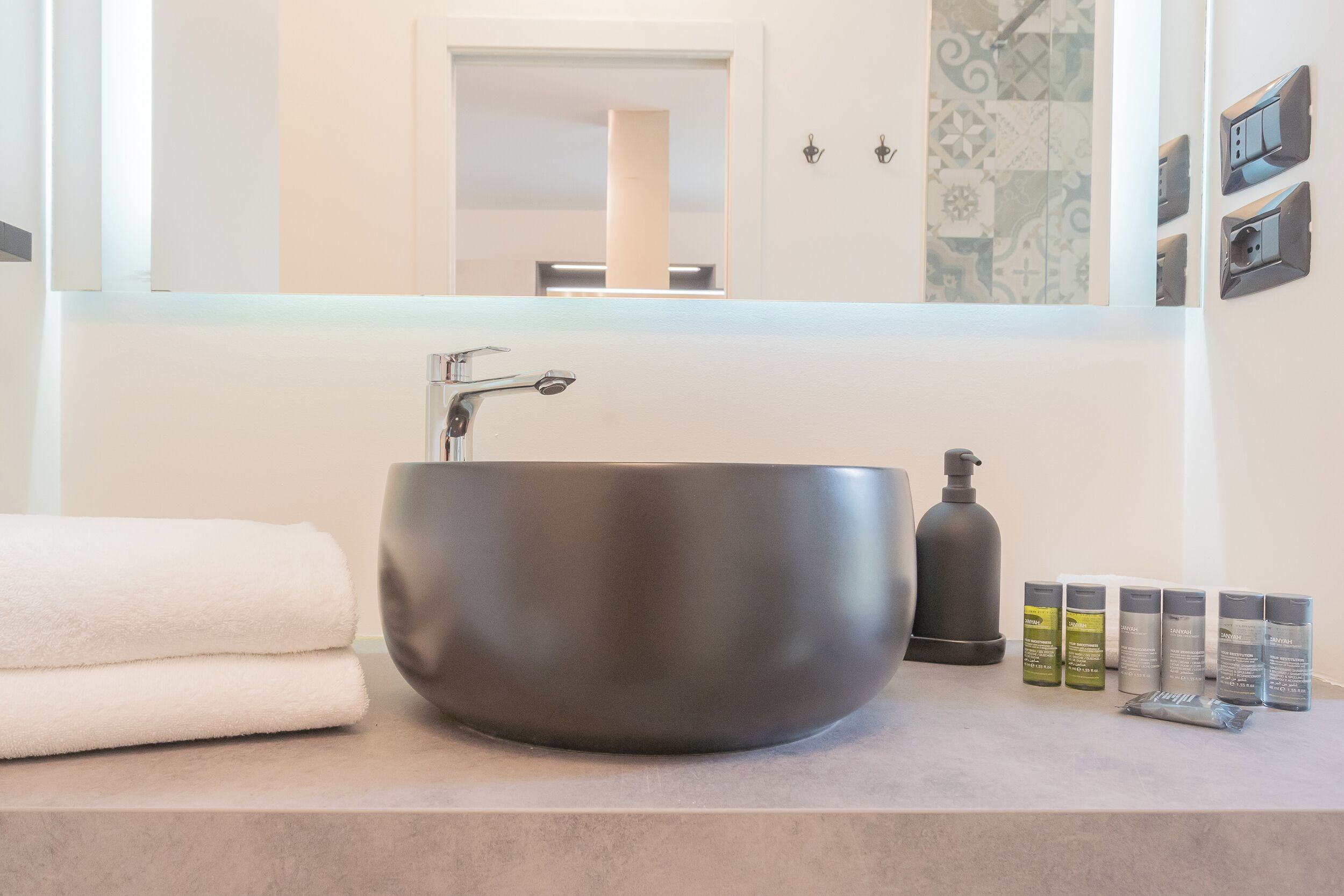 Un baño moderno con un lavamanos grande, redondo y de color oscuro, un espejo y toallas blancas dobladas con cuidado.