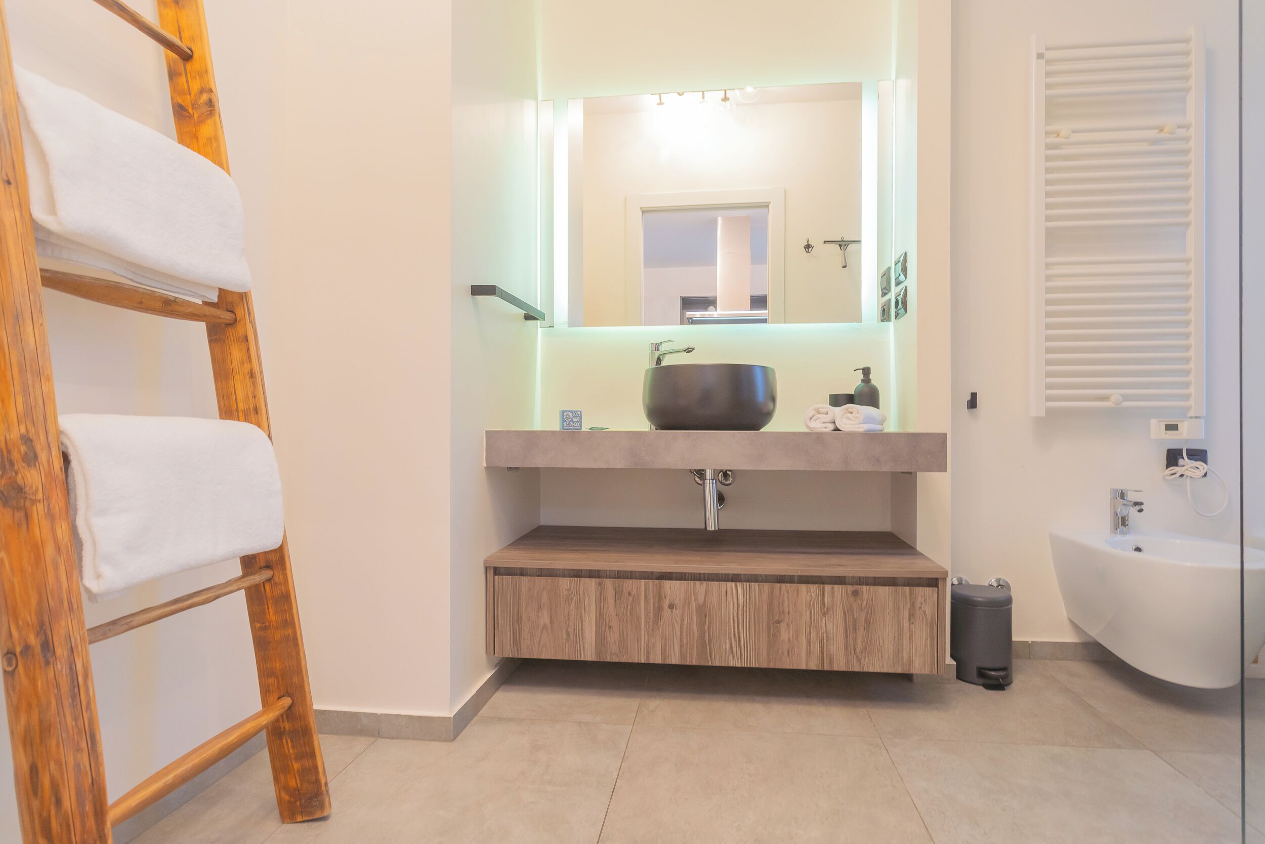 A modern bathroom with a wooden vanity, a large mirror, a freestanding bathtub, and a towel rack.