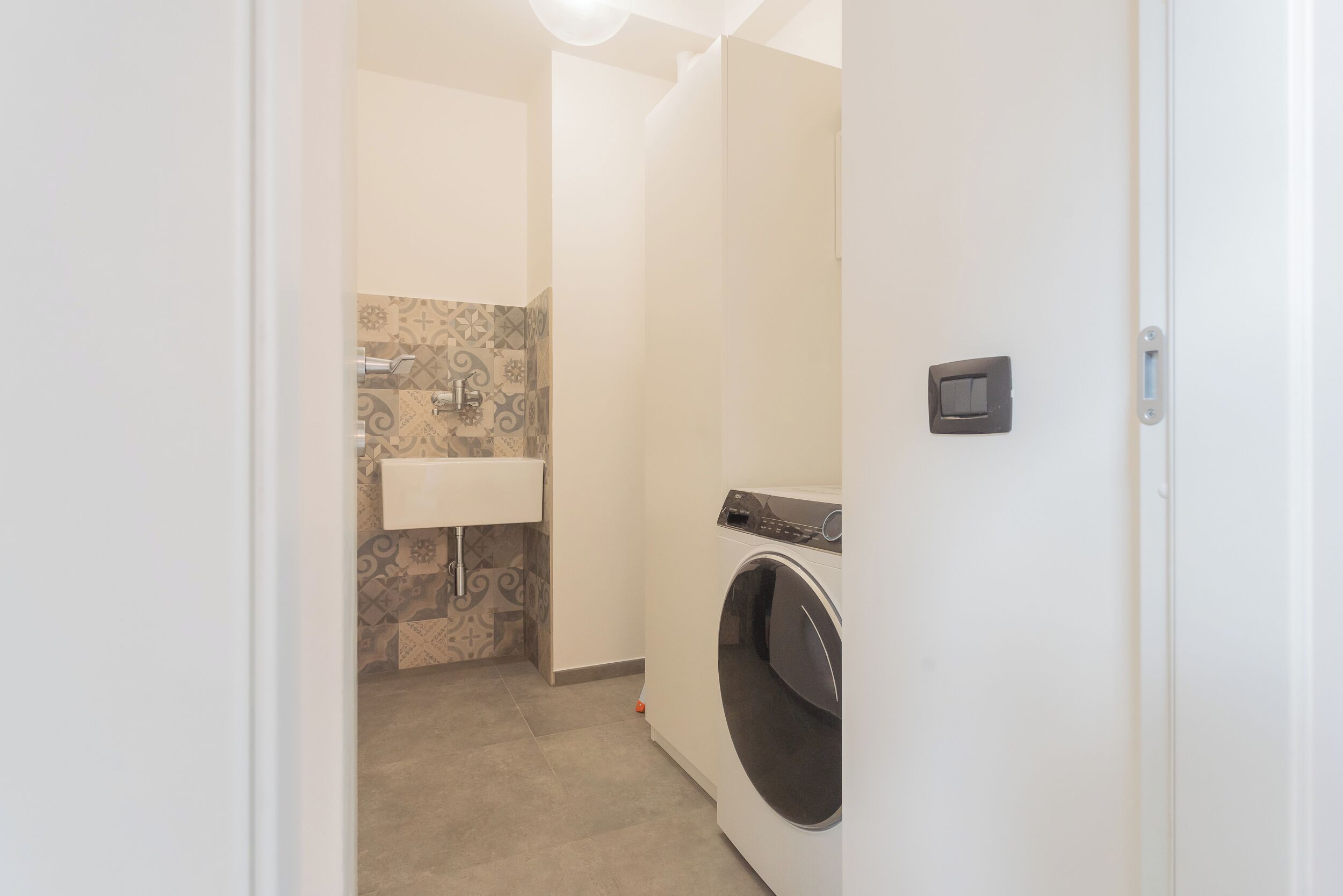 A laundry room with a washing machine, a sink, and patterned tiles.