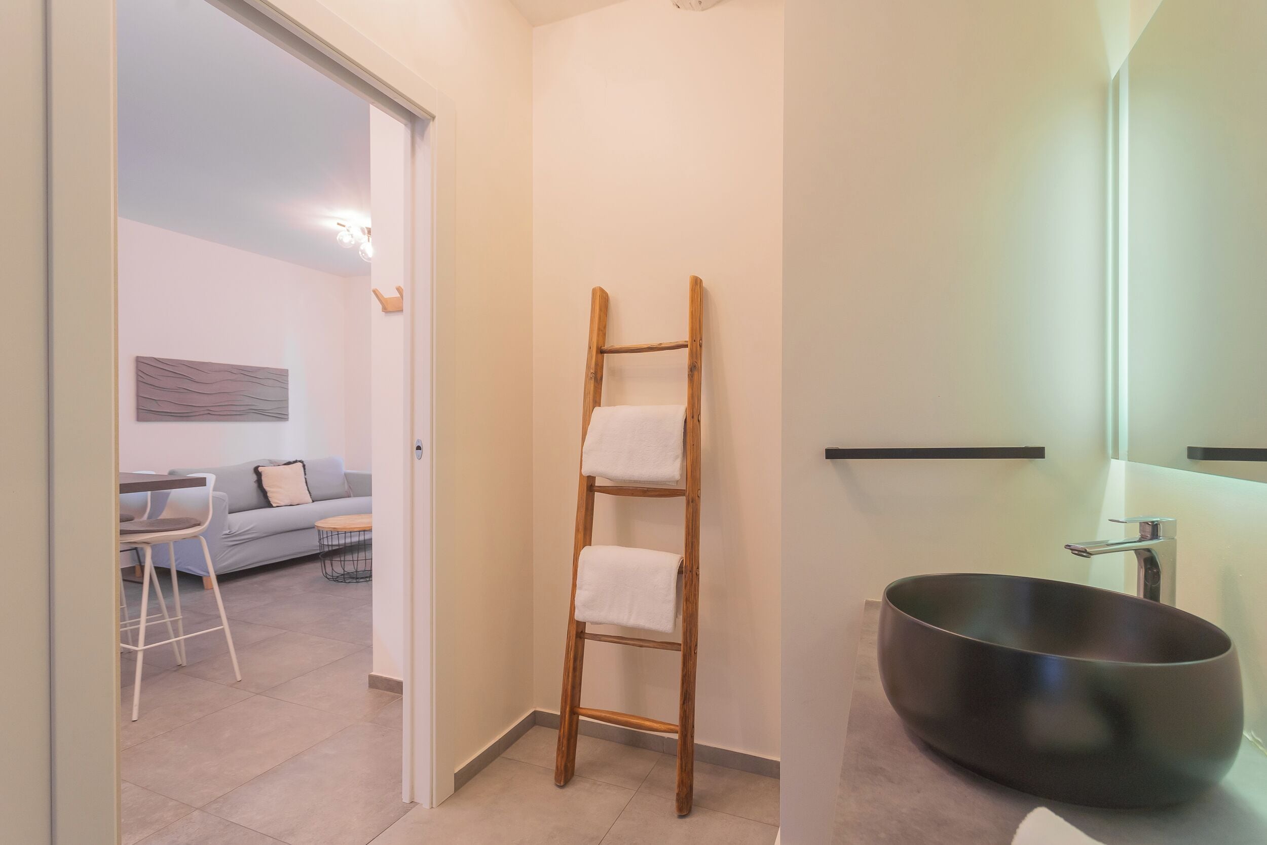 Un baño con una escalera de madera, un lavabo negro y un sofá gris en la zona de estar contigua.