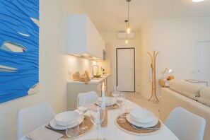 Un comedor moderno con una mesa preparada para cuatro personas, una cocina al fondo y un sofá en la sala de estar.