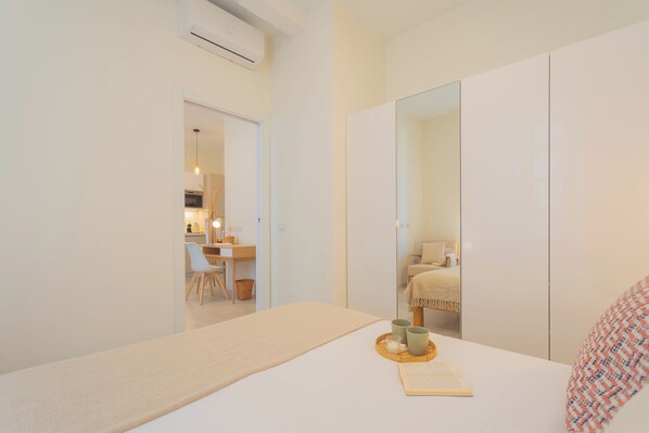 Un dormitorio minimalista con cama, mesita de noche y un espejo grande.