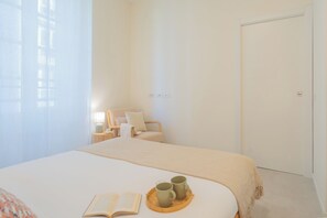 Un dormitorio con cama, mesita de noche, lámpara, silla y una puerta.