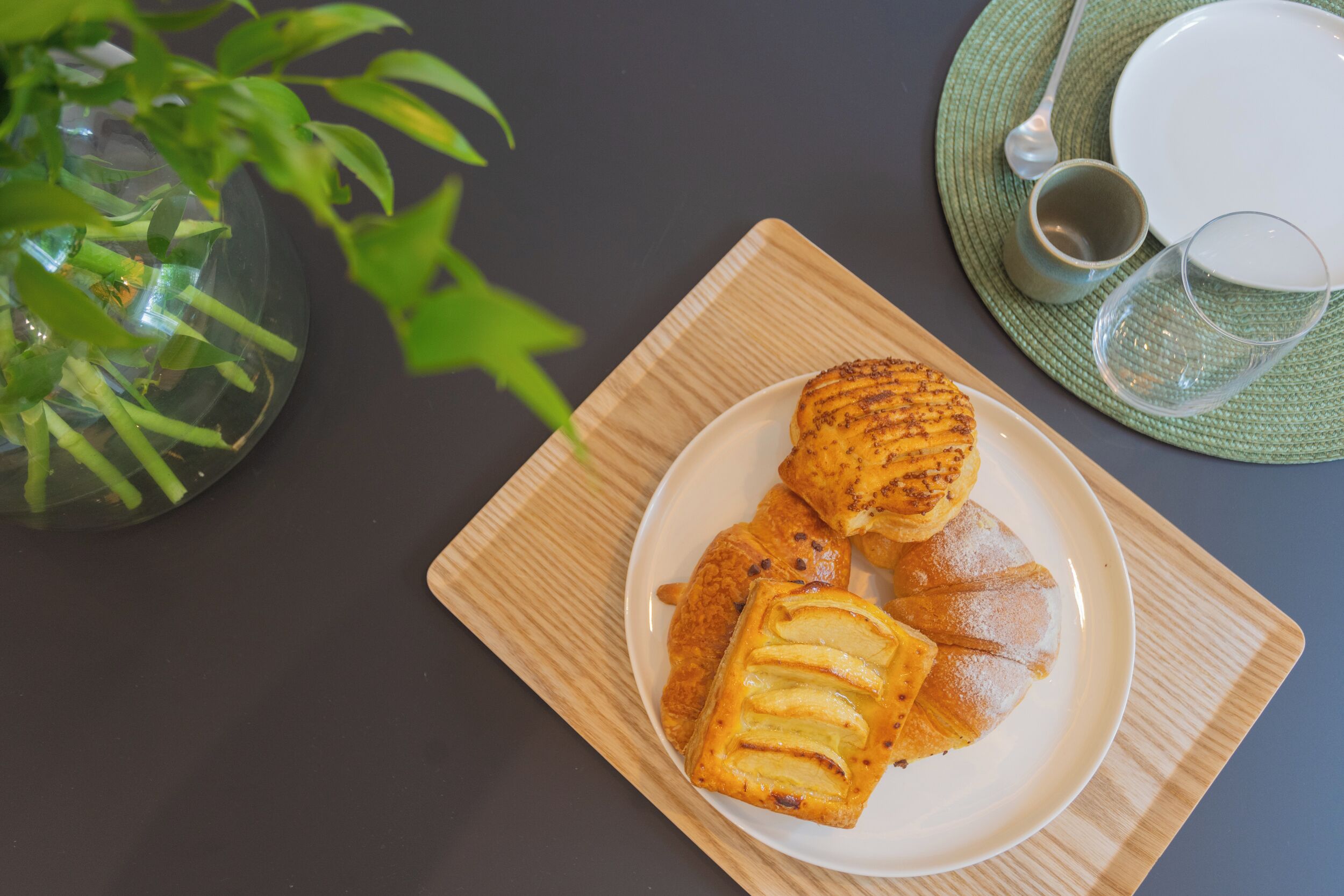 Un plato de pasteles sobre una bandeja de madera, un vaso de agua y una taza en una mesa con un mantel individual verde.