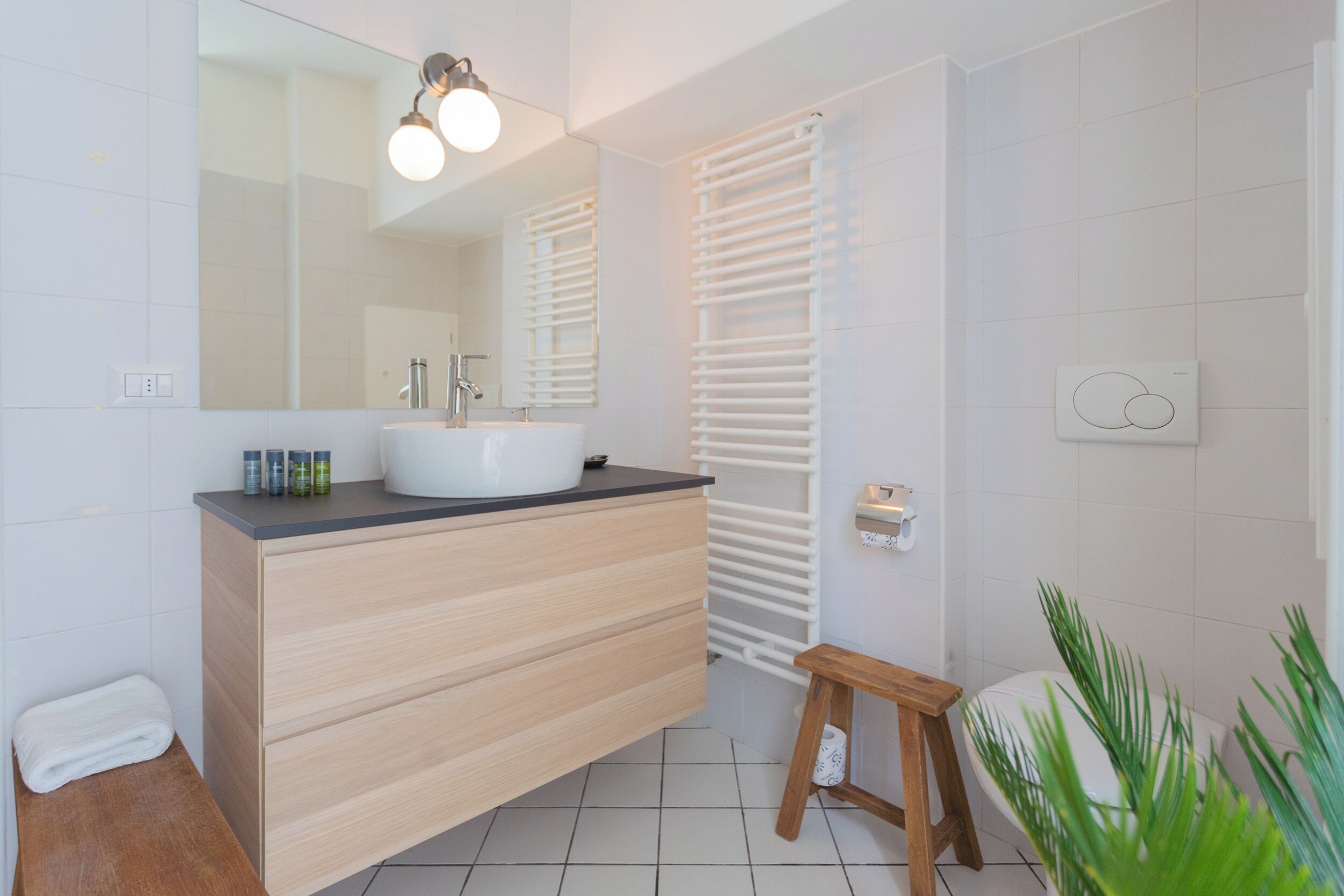 Une salle de bain moderne avec un grand miroir, un lavabo et un tabouret en bois.