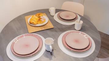 Una mesa redonda con platos rosa y blancos, una tabla de madera con pasteles y dos tazas blancas.