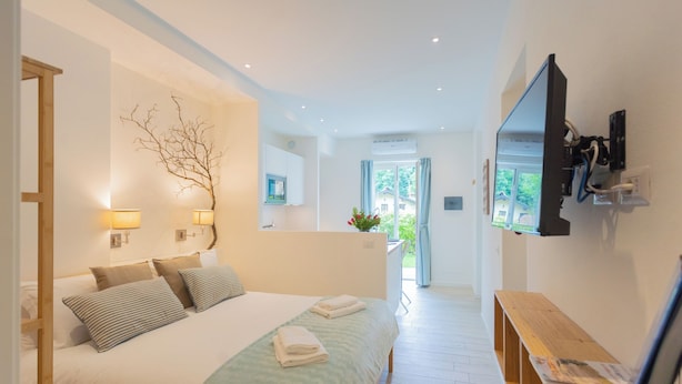 Un dormitorio moderno con una cama grande, lámparas de noche, un televisor montado en la pared y un banco de madera.