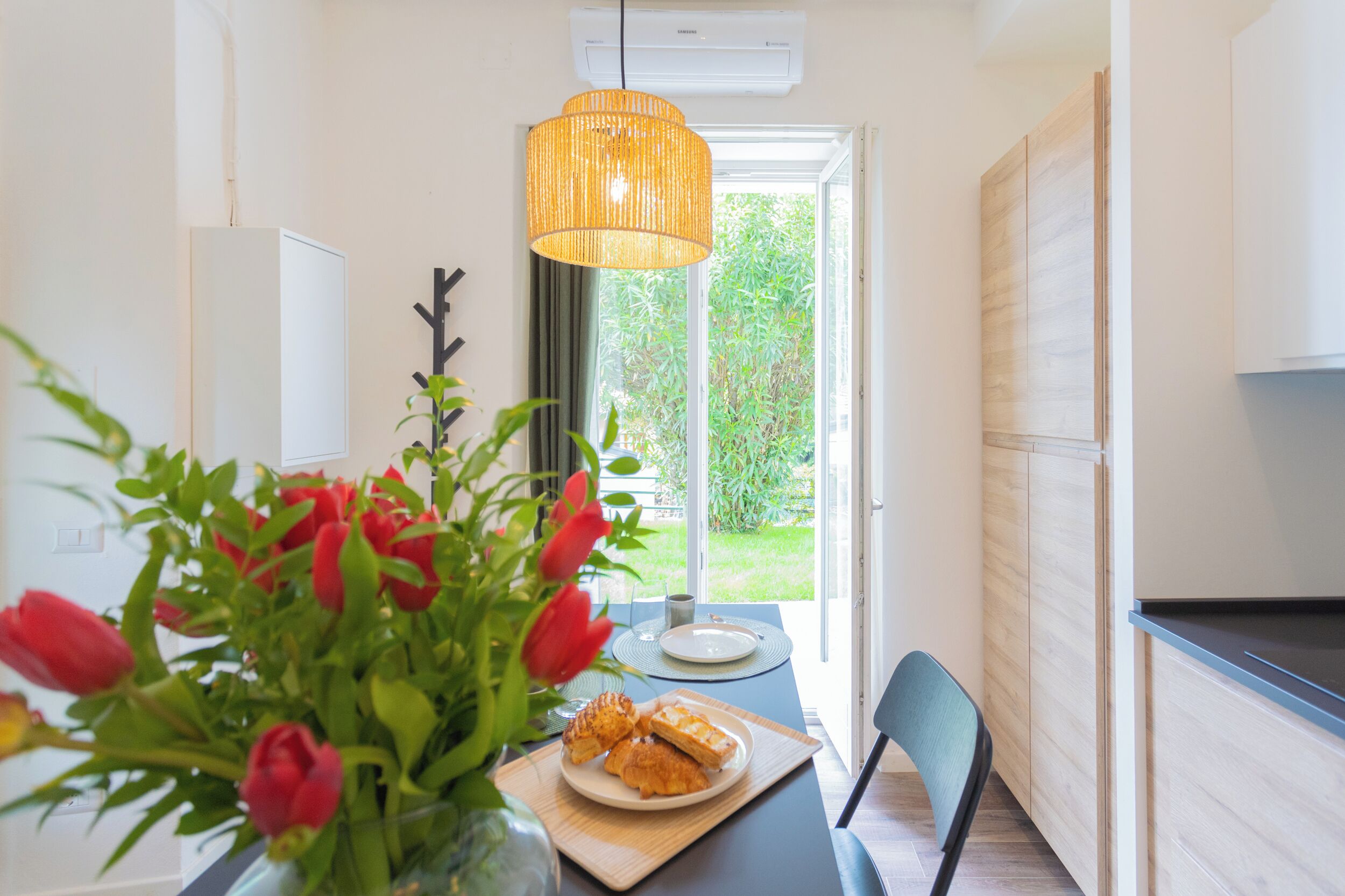 A modern kitchen with a dining area, featuring a table with a plate of pastries and a vase of red tulips.