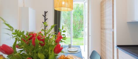 A modern kitchen with a dining area, featuring a table with a plate of pastries and a vase of red tulips.