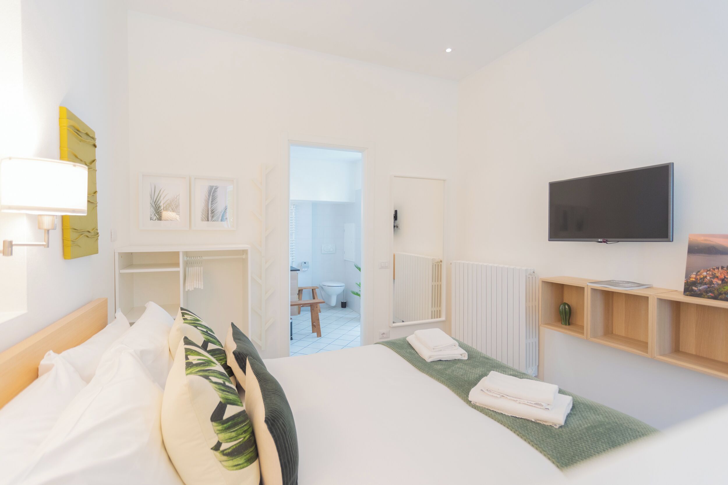 A modern hotel room with a bed, a TV, a small desk, and a view of the bathroom.