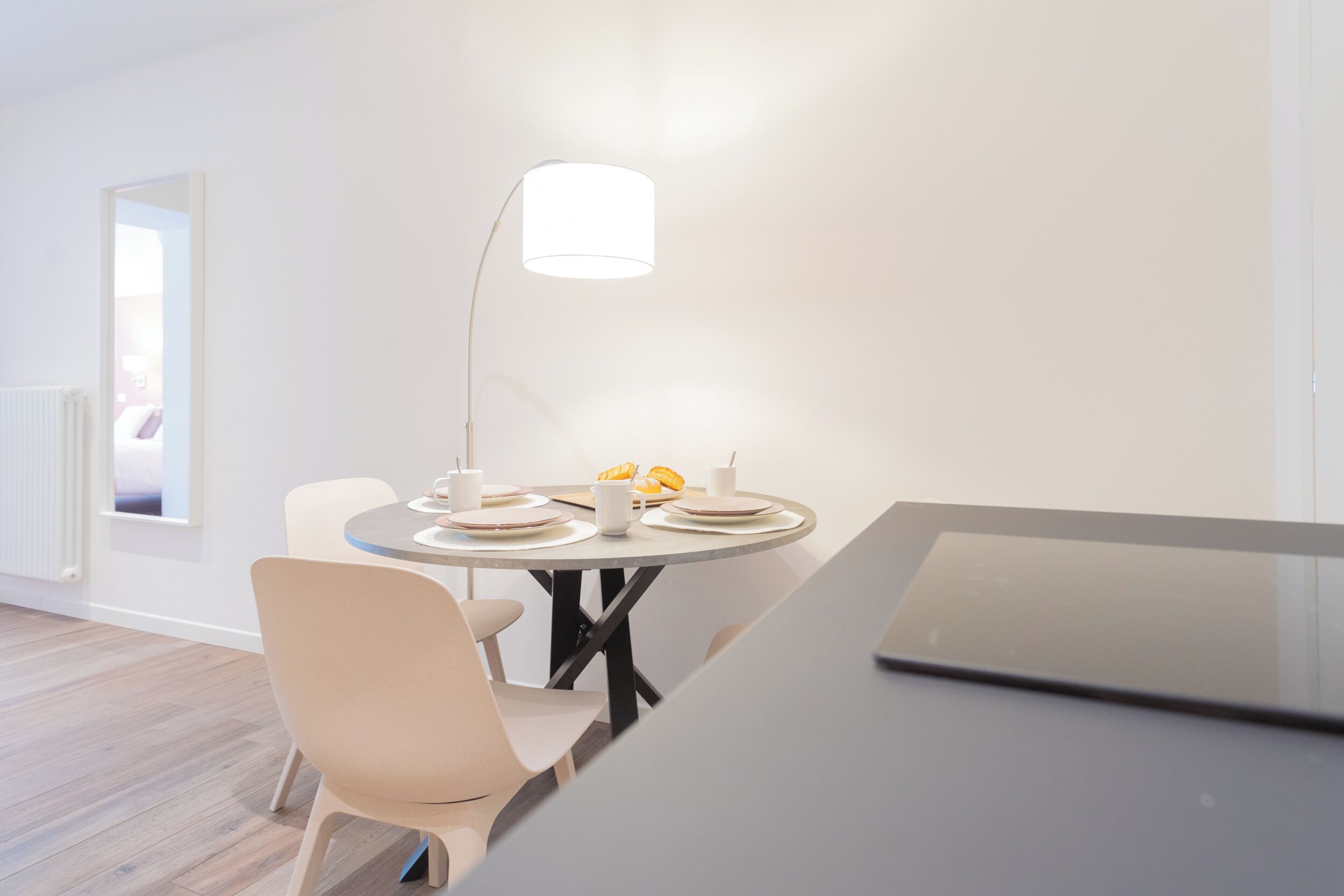 A modern dining area with a round table, white chairs, and a minimalist lamp.