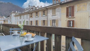 A balcony with a table set for breakfast, including croissants and orange juice, overlooking a row of buildings with decorative facades and a mountain in the background. - Garibaldi's Balcony by Rent all Como (Como)