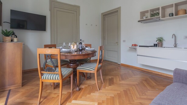 A dining area with a round table set for four, surrounded by wooden chairs with striped cushions. A television is mounted on the wall above the table. - Garibaldi's Balcony by Rent all Como (Como)