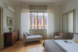 A bedroom with a bed, a chair, a dresser, and a window with a view of buildings. - Garibaldi's Balcony by Rent all Como (Como)