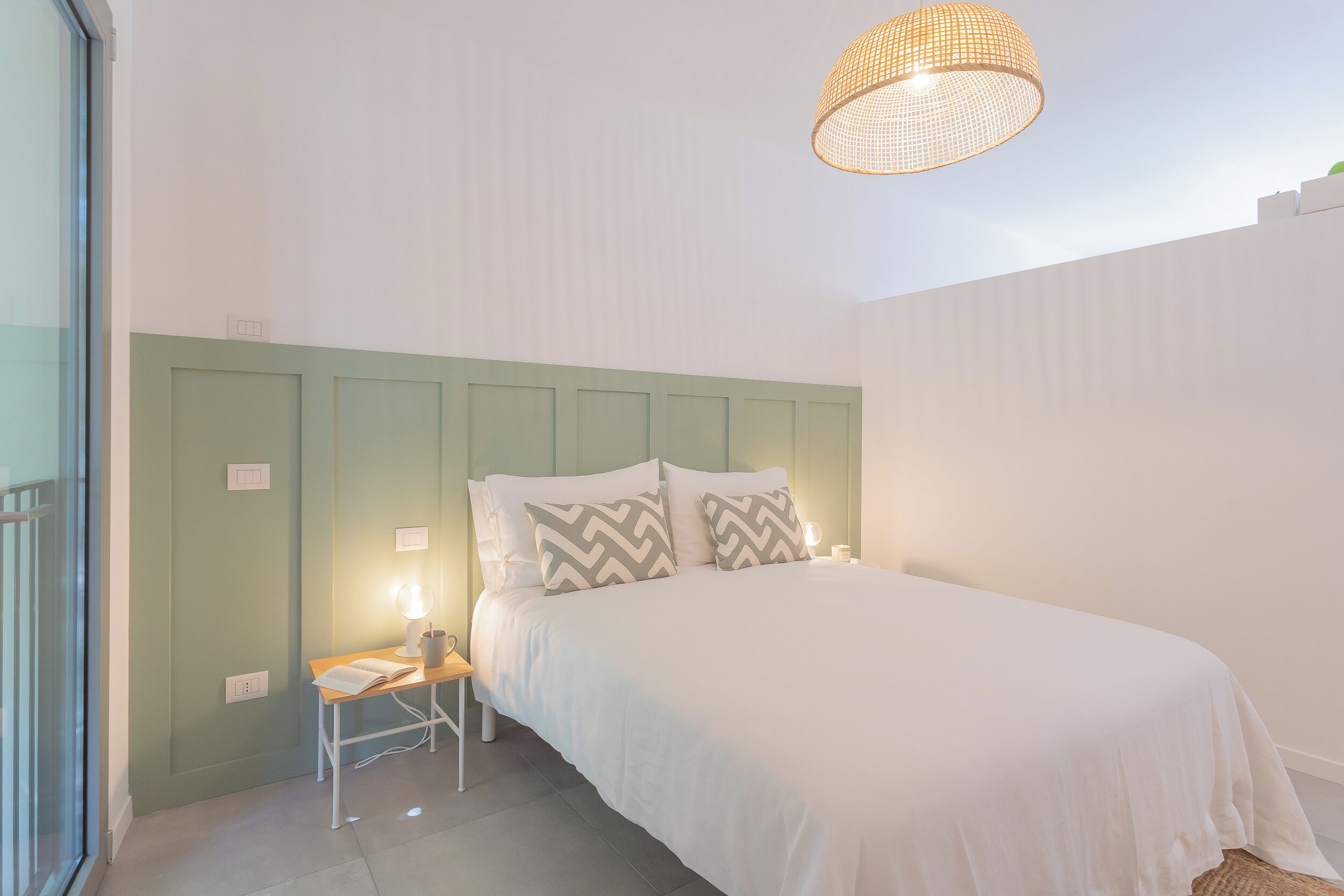 Ein Schlafzimmer mit Bett, Nachttisch, Lampe und einer Hängeleuchte.