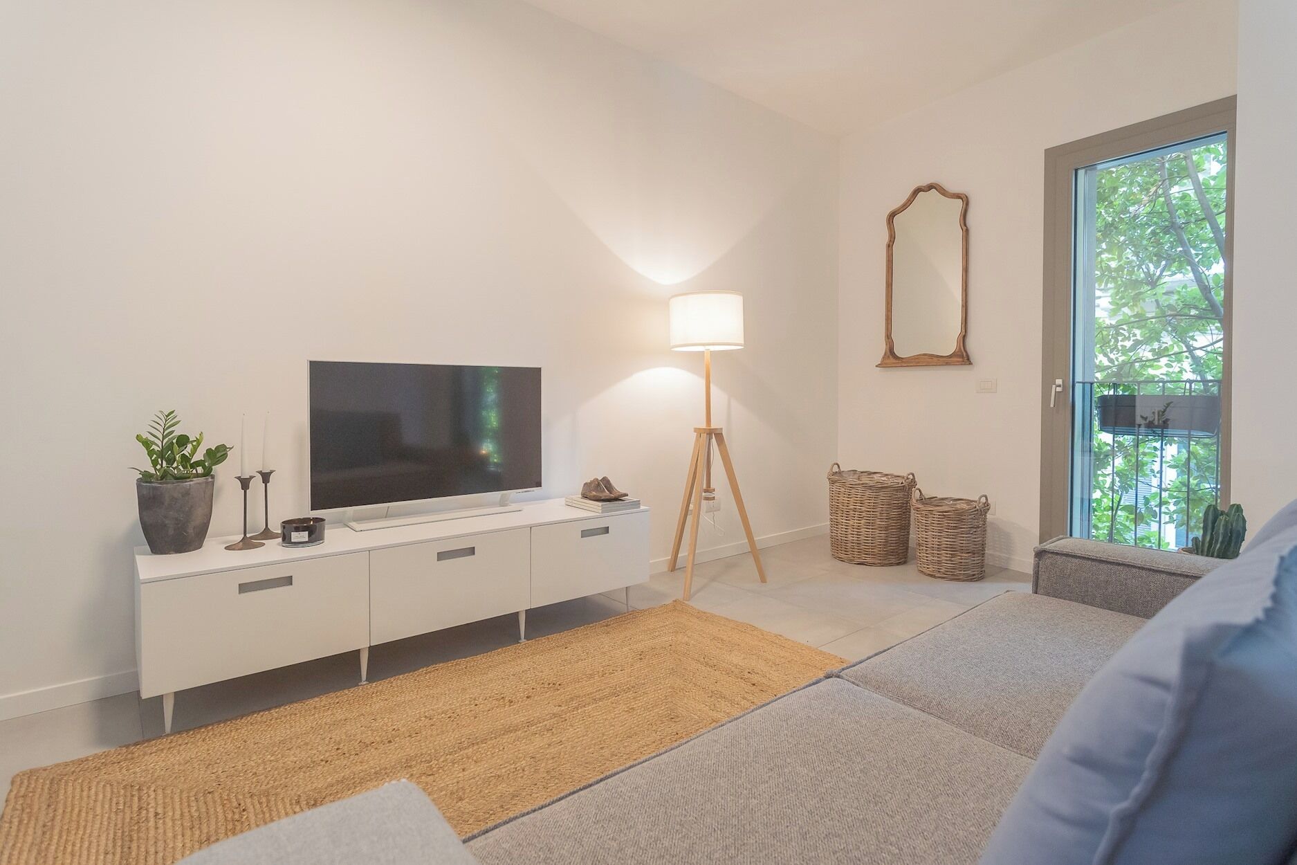Un salon moderne doté d’un téléviseur à écran plat, d’un lampadaire, d’une grande fenêtre et offrant une vue sur la verdure environnante.