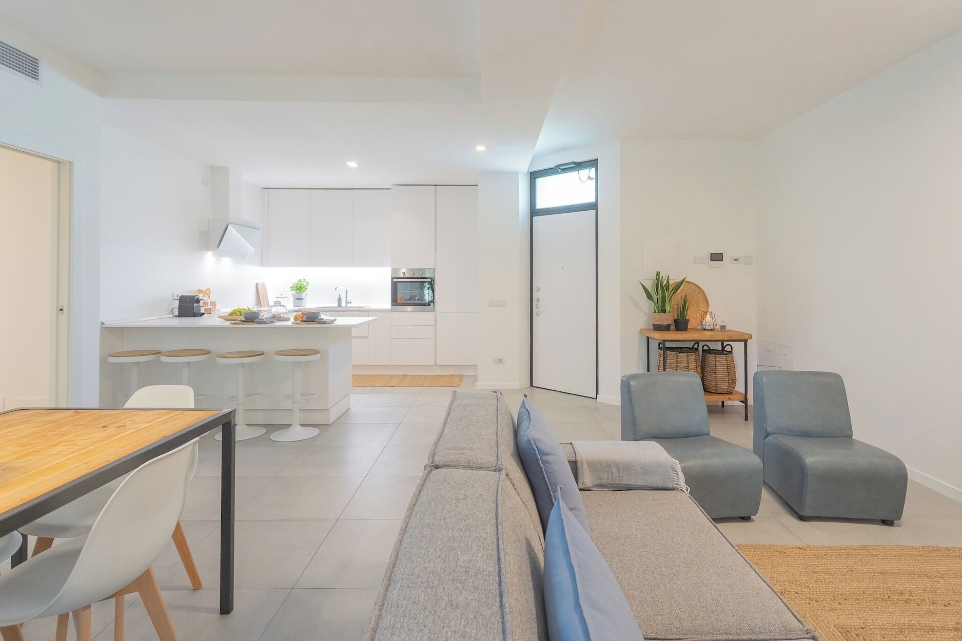 Ein modernes Wohnzimmer mit Sofa, einem Esstisch mit Stühlen und einer Küchenzeile mit Kochinsel und Barhocker.
