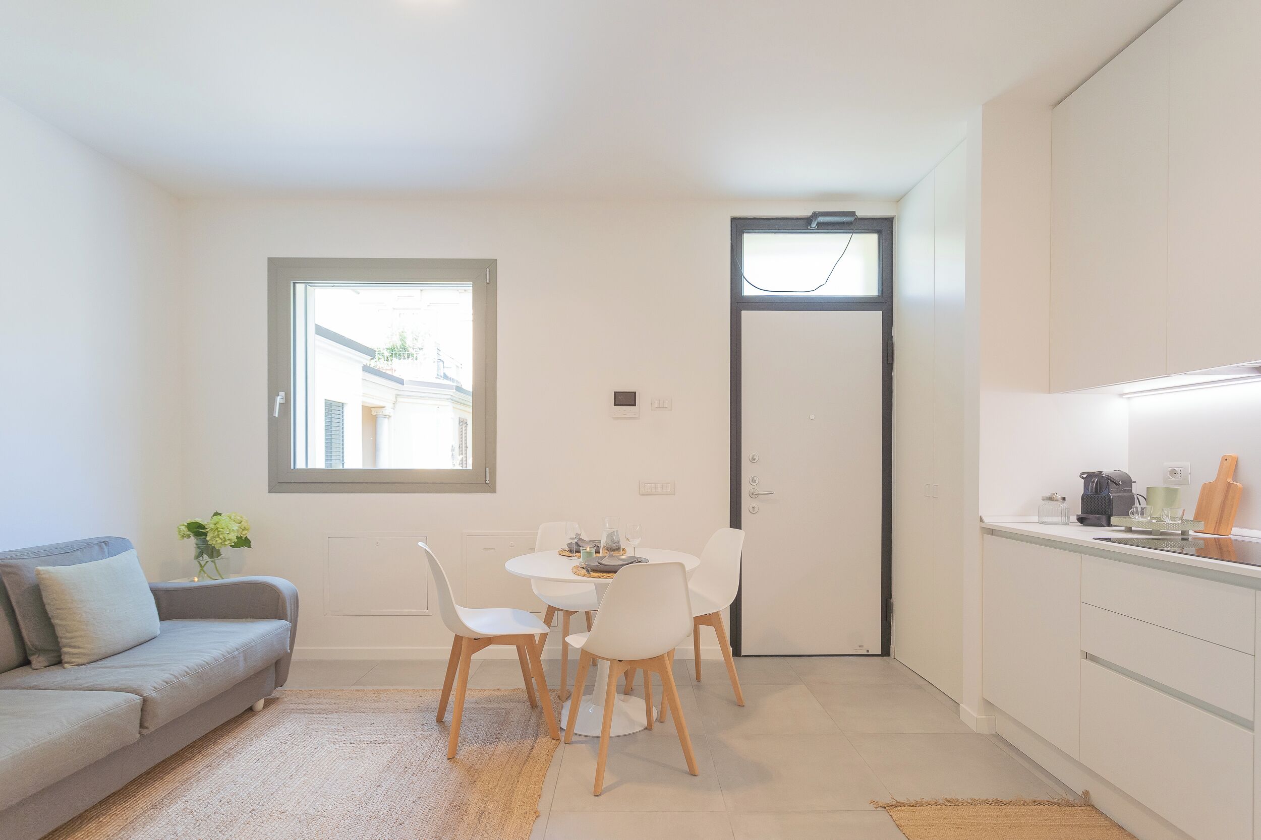 A compact living space with a sofa, dining table, chairs, a small kitchen area, and a door.
