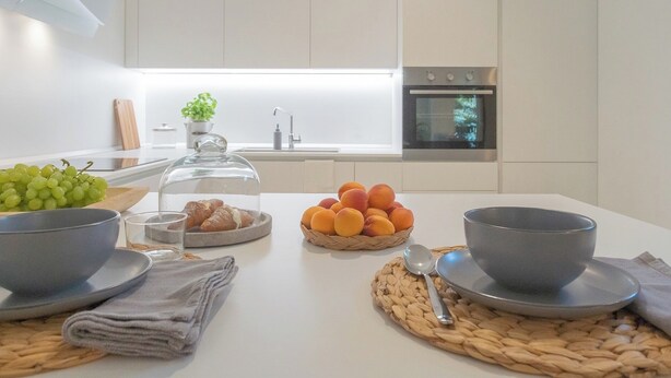A modern kitchen with a white countertop, a sink, and an oven. There are bowls, a basket of oranges, and a glass container with bread. - Salvia & Ginepro Apartments by Rent all Como (Como)