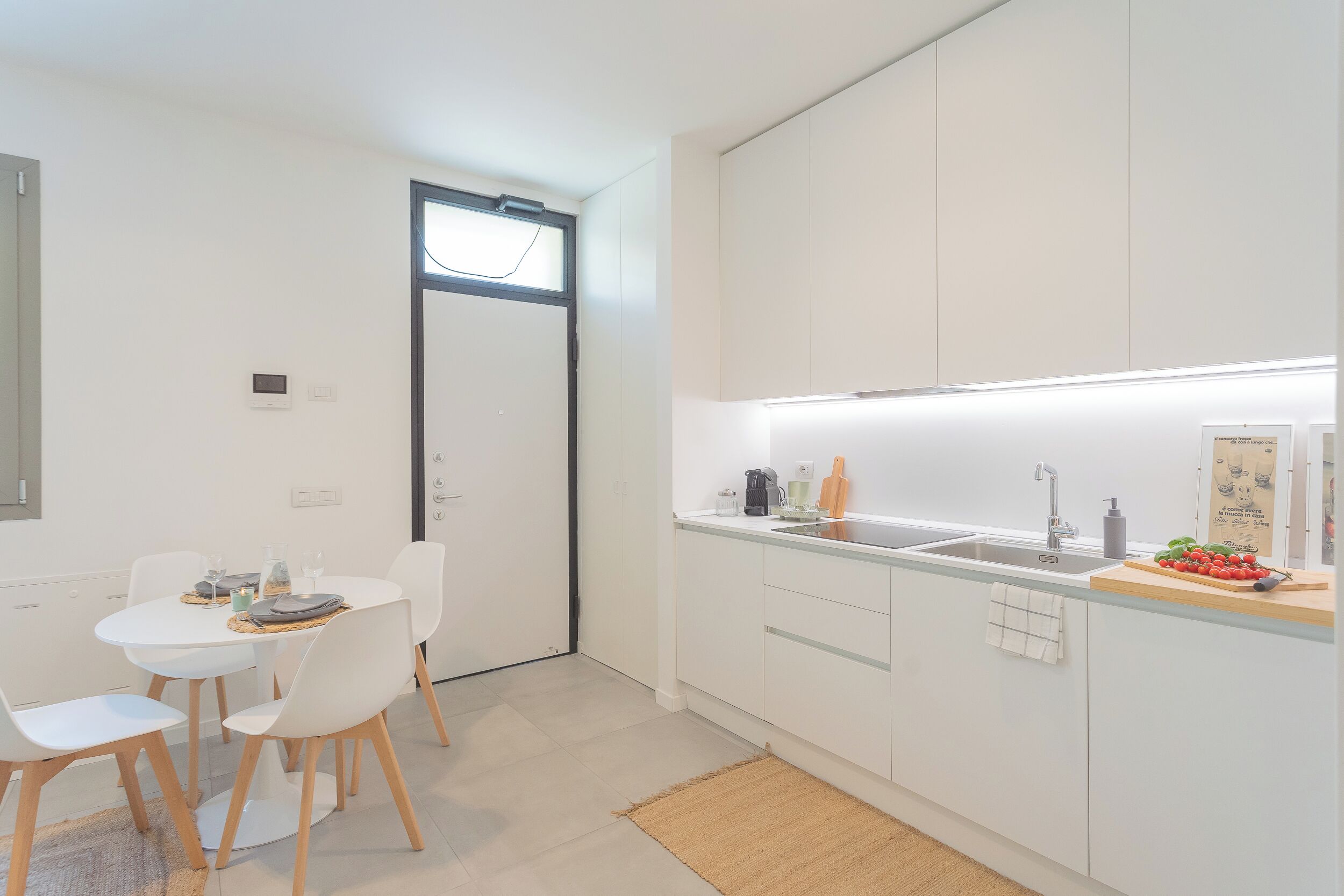 A modern kitchen with white cabinets, a central island, and a dining area with white chairs.