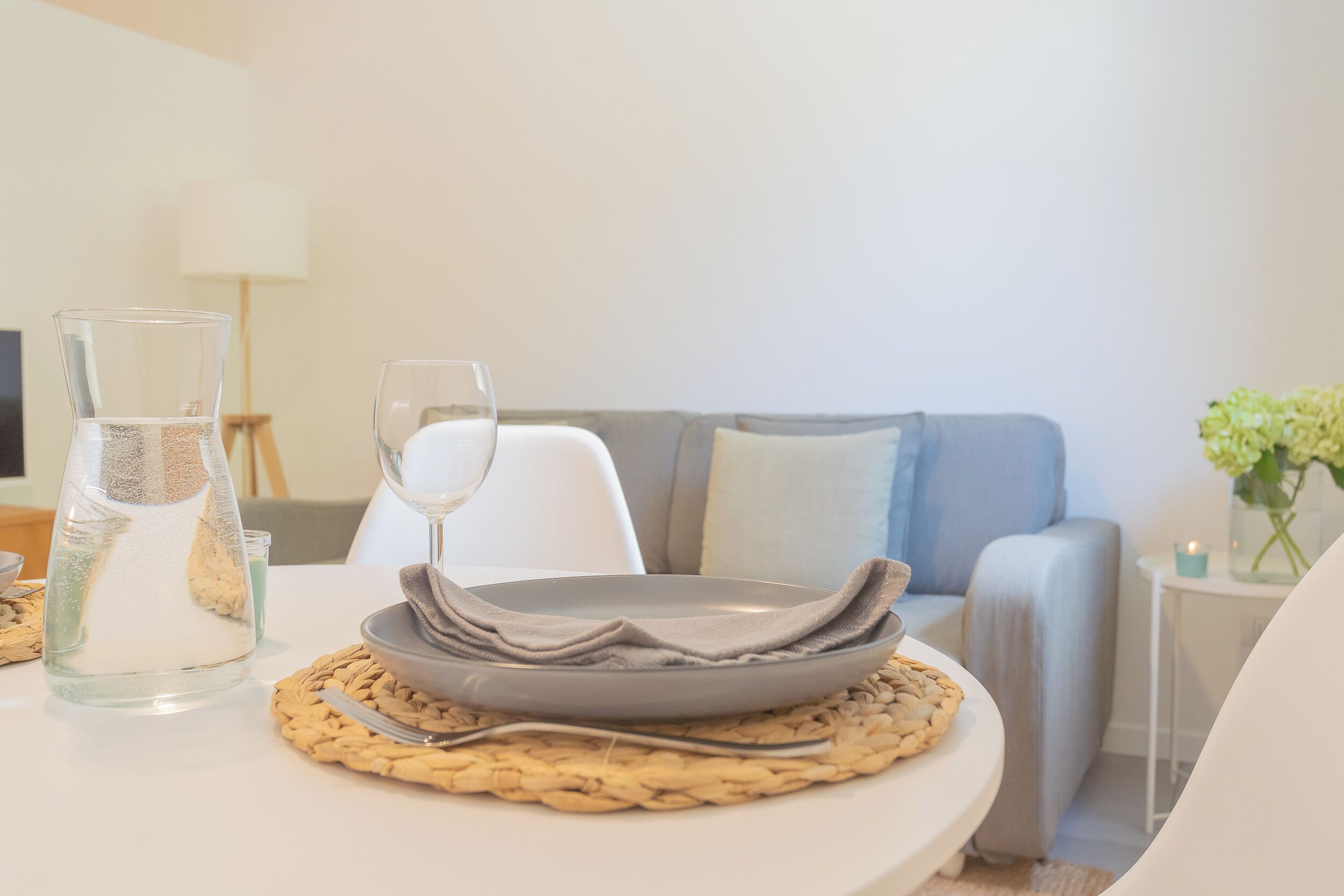 A dining table with a glass pitcher, a wine glass, and stacked plates on a woven placemat.