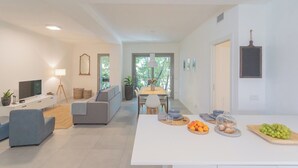 A modern living room with a flat-screen TV, a sofa, a dining table with chairs, and a kitchen area with a counter displaying fruits and pastries. - Salvia & Ginepro Apartments by Rent all Como (Como)