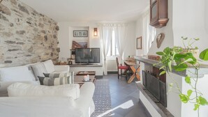 A cozy living room with a stone wall, a television, a fireplace, and a dining area. - Giuliano's House - Amazing Lake View by Rent all Como (Laglio)