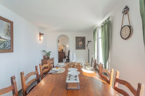 A dining area with a wooden table set for six, surrounded by wooden chairs. A painting and a clock are on the walls. - Giuliano's House - Amazing Lake View by Rent all Como (Laglio)