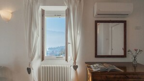 A room with a window, an air conditioner, a mirror, and a wooden dresser with a magazine. - Giuliano's House - Amazing Lake View by Rent all Como (Laglio)