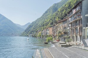A lakeside building with balconies, a stone pathway, and a view of the lake and mountains. - Il Timone by Rent all Como (Colonno)