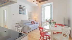 A modern living space with a sofa, dining table, and chairs. There is a painting on the wall, a window with natural light, and a kitchen area. - Independence Apartment With Balcony by Rent all Como (Como)
