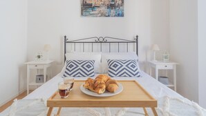 A neatly made bed with patterned pillows, a tray with croissants and coffee, and a painting of a canal scene on the wall. - Independence Apartment With Balcony by Rent all Como (Como)