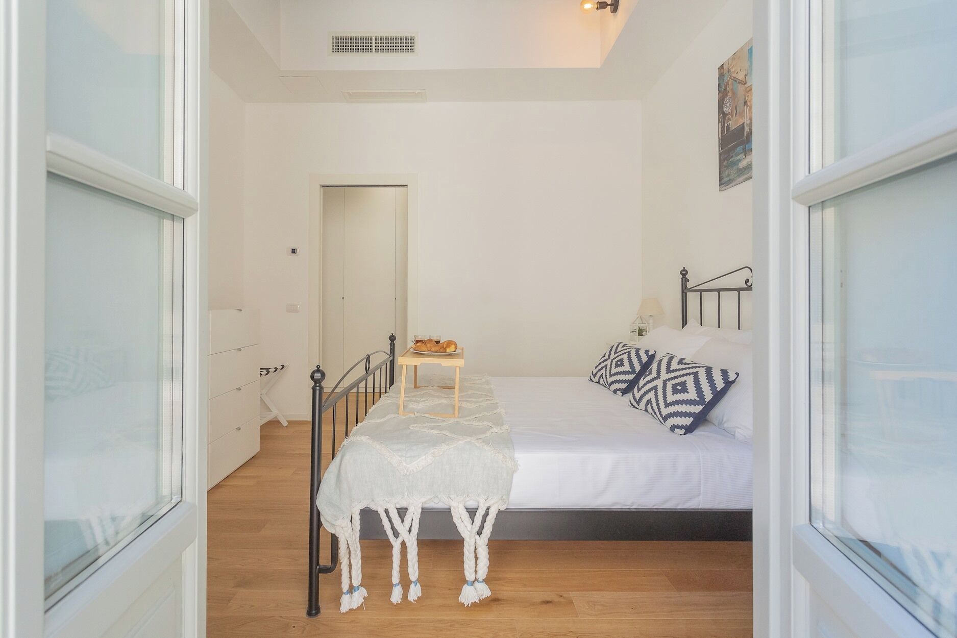 A bedroom with a bed, a small table with a lamp, and a window.