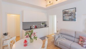 A modern kitchen with white cabinets, a dining area with a round table, and a grey sofa. - Independence Apartment With Balcony by Rent all Como (Como)