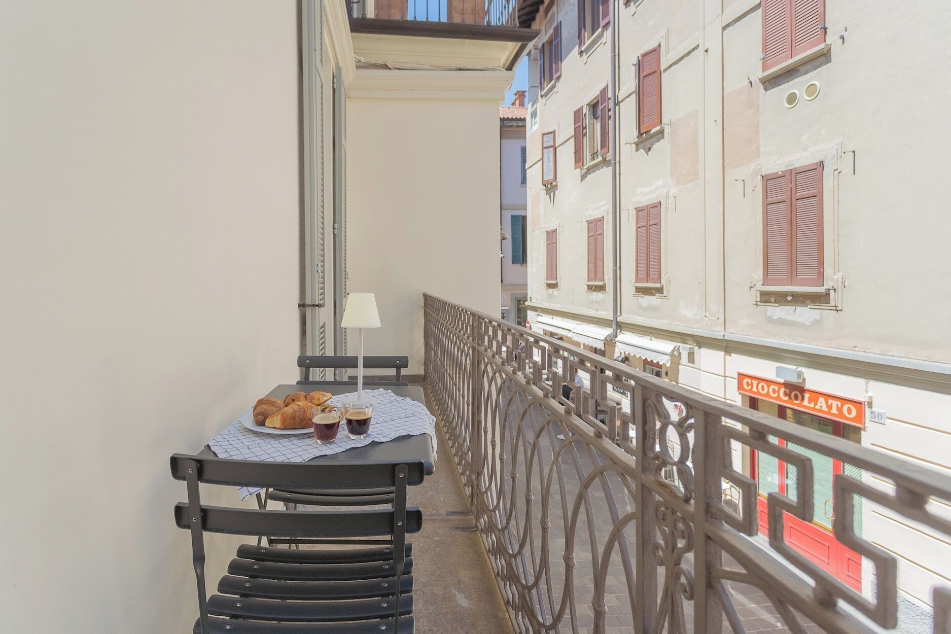 A balcony with a table set for two, featuring croissants and a cup of coffee.