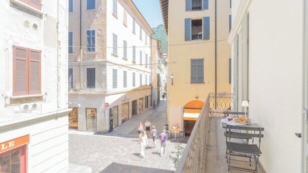 A narrow street with buildings on both sides, a café with outdoor seating, and a few pedestrians. - Independence Apartment With Balcony by Rent all Como (Como)