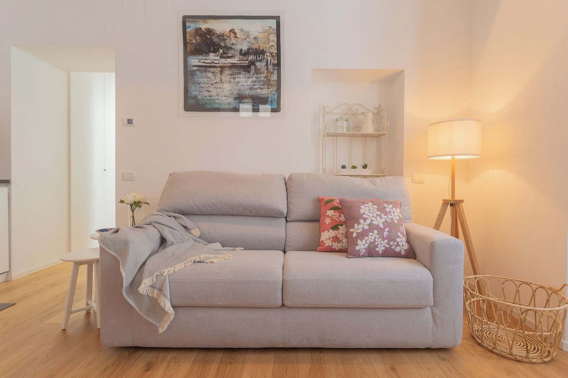 A living room with a light grey sofa, a small white table, a floor lamp, and a wicker basket.