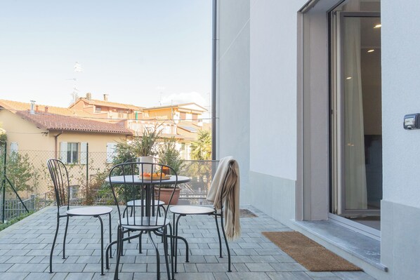 A balcony with a table and chairs, a potted plant, and a view of neighboring buildings.