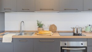 A modern kitchen with grey cabinets, a stainless steel sink, a wooden countertop, a loaf of bread, a potted plant, a woven basket, and a kettle. - Isola Felice Grandate by Rent all Como (Grandate)