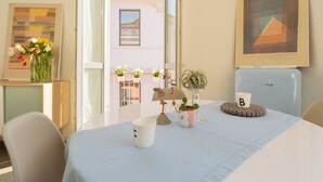A room with a table set with a blue tablecloth, a white mug, a small potted plant, and a decorative item. There is a framed picture on the wall and a window with a view of buildings outside. - Via Anzi Como Apartments by Rent all Como (Como)