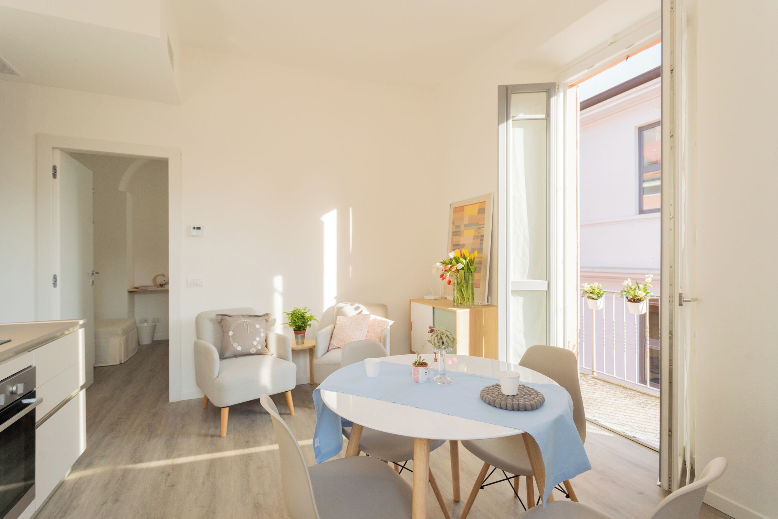 A modern living room with a round table, light-colored furniture, and a view of the outside balcony.