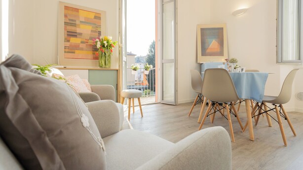 A modern living room with a sofa, a dining table with chairs, and a view of the outside through a glass door. - Via Anzi Como Apartments by Rent all Como (Como)