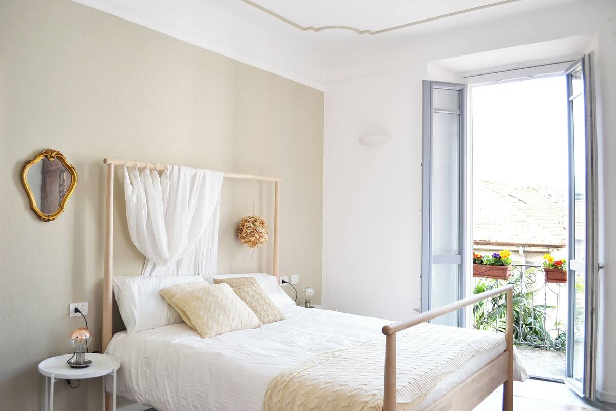 A bedroom with a bed, bedside tables, a mirror, and a view of the outside.