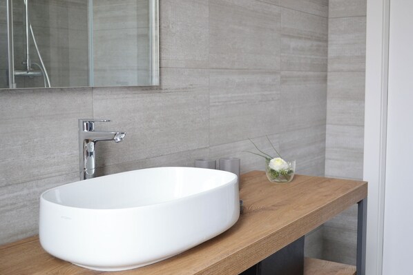 A modern bathroom with a white oval sink, a wooden vanity, and a mirror above the sink.