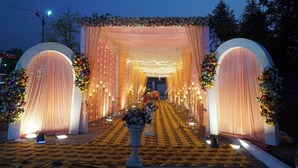 Un espacio exterior decorado para un evento, con un sendero alfombrado, arreglos florales y cortinas colgantes.