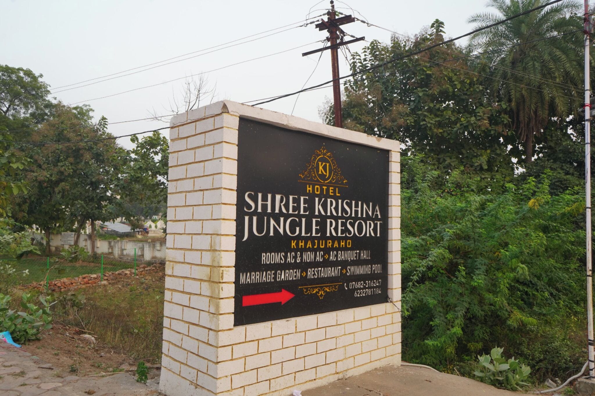 A sign for Shree Krishna Jungle Resort, highlighting amenities like rooms, a banquet hall, a marriage garden, a restaurant, and a swimming pool.