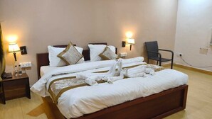 Una cama bien hecha con ropa de cama blanca y detalles dorados, dos lámparas de noche, una silla y un enchufe de pared.