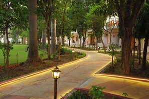 A curved pathway lined with trees and illuminated by ground lights, leading to a building with a traditional architectural style. - Hotel Shree Krishna Jungle Resort (Rajnagar)