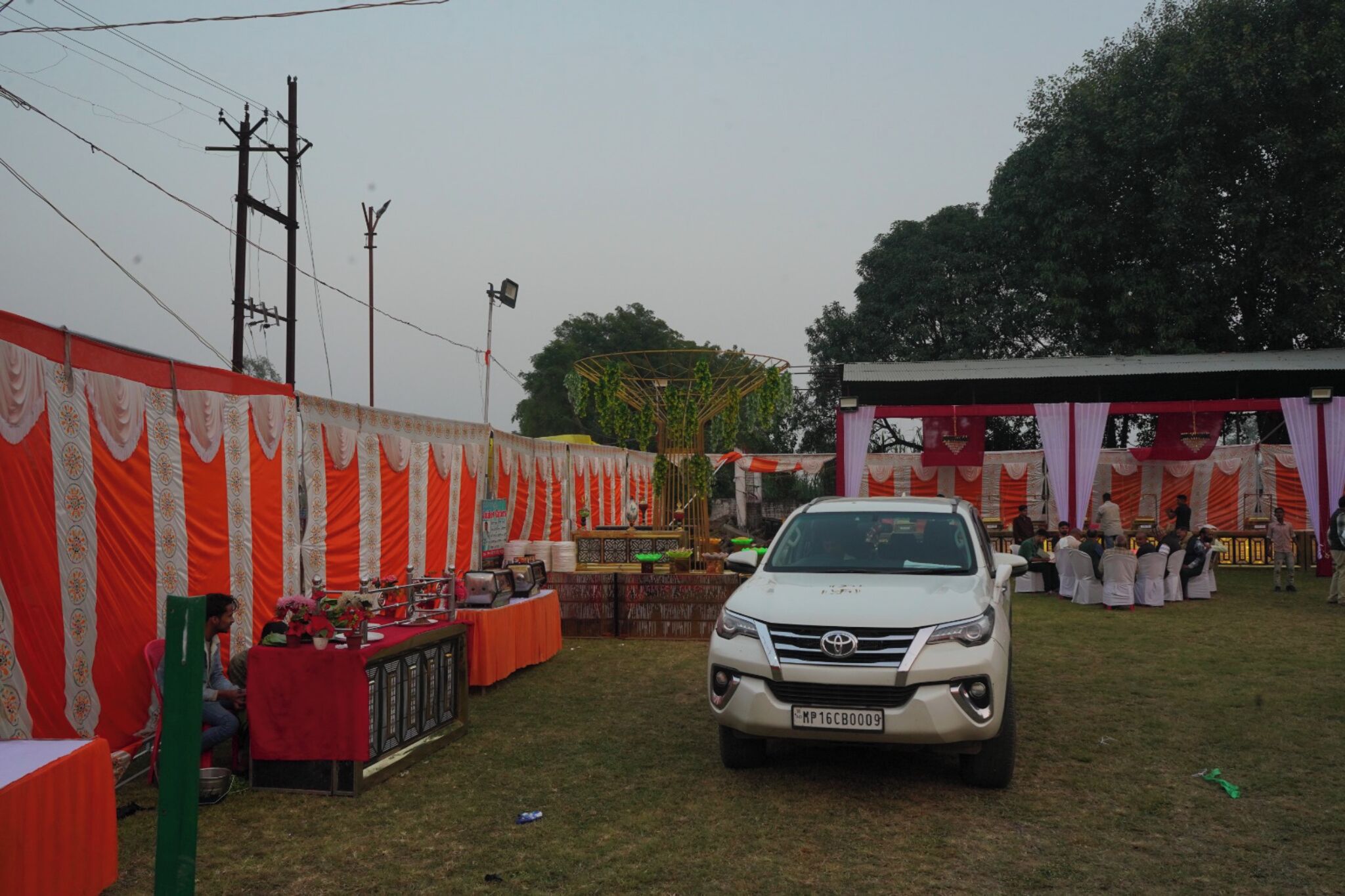 A white SUV parked in a grassy area with a tented event space in the background.