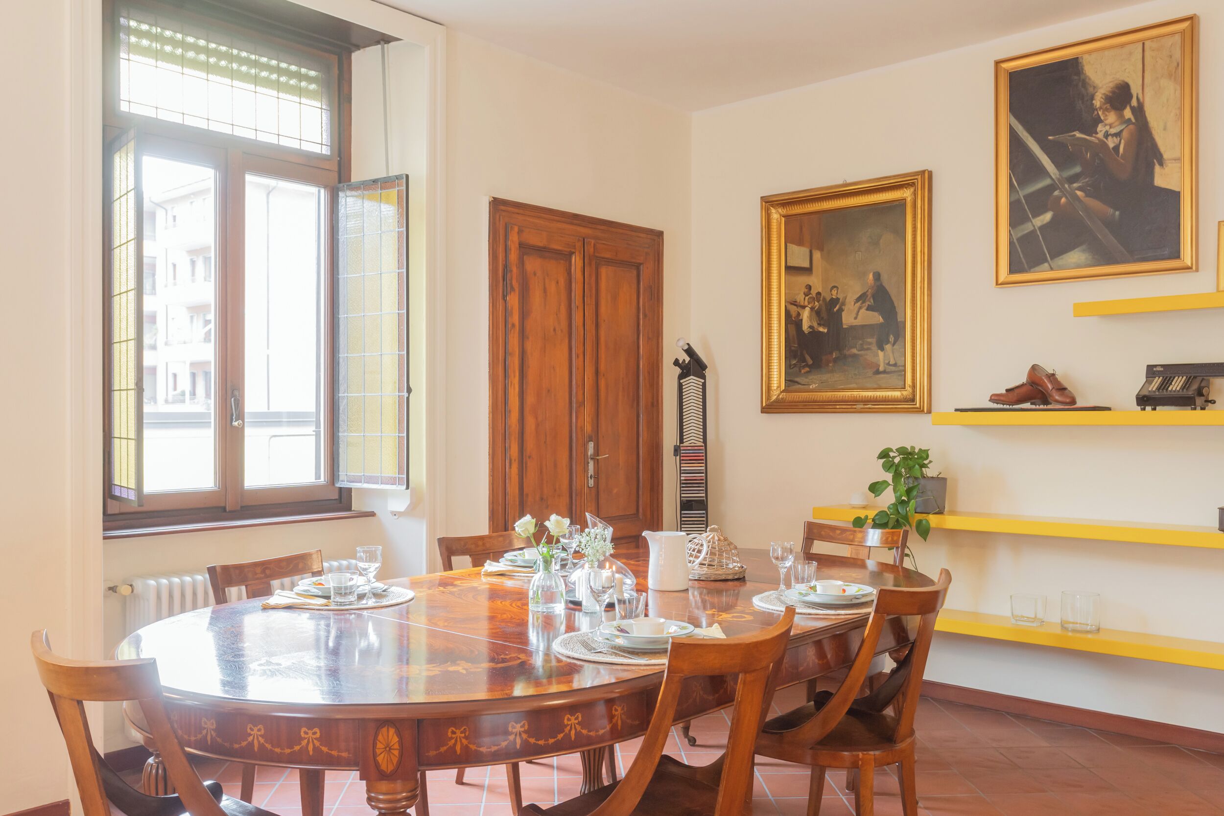 A dining area with a round wooden table, chairs, and a window with blinds.